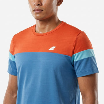 A man is seen wearing the Babolat Crew Neck Mens Tennis T-Shirt - Seaport, a color-blocked tee by Babolat featuring an orange top, blue middle section, and light blue stripes on the sleeves, with a small white logo on the chest. Only his upper body and part of his face are visible in this classic crew neck tennis shirt.