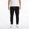 A person wearing a white t-shirt, Babolat Play Men’s Tennis Pants in black featuring a small white Babolat logo on the left leg, and white sneakers stands against a plain white background.