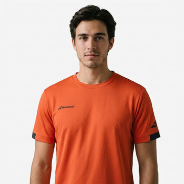 A man with short brown hair wears a Babolat Play Mens Crew Neck Tennis T-Shirt in Fiesta Red and stands against a plain white background, looking directly at the camera with a neutral expression.
