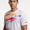 A man is wearing the HEAD Blur Mens Tennis T-Shirt - PUXU by HEAD—a white tennis shirt accented with vibrant orange, purple, and pink abstract streaks and a subtle logo on the chest. Designed with moisture-wicking fabric for comfort, the t-shirt also features a “HEAD” logo on the sleeve. The background is plain white.