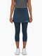 A woman stands against a plain white background wearing a grey short-sleeve top, white sneakers, and the HEAD Club 3/4 Tights Women’s Tennis Skort in navy. The skort, featuring the HEAD logo, is crafted from moisture transfer microfibre to keep you cool and comfortable on and off the court.