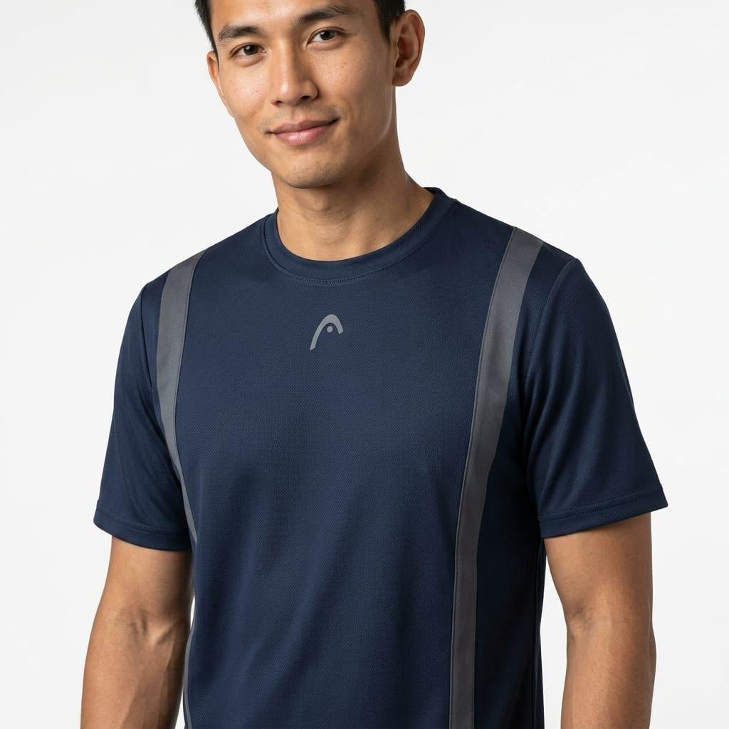 A man stands against a plain white background, smiling slightly, wearing the HEAD Club Tech 25 Mens Tennis T-Shirt in navy by HEAD. This shirt features gray vertical stripes and a small logo, and is made from breathable moisture transfer microfiber for comfort on and off the court.