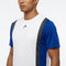 A man wearing the HEAD Club Tech 25 Men’s Tennis T-Shirt in royal blue and white—a short-sleeved sports shirt crafted from moisture transfer microfiber, featuring blue sleeves and black vertical stripes—stands against a plain white background.