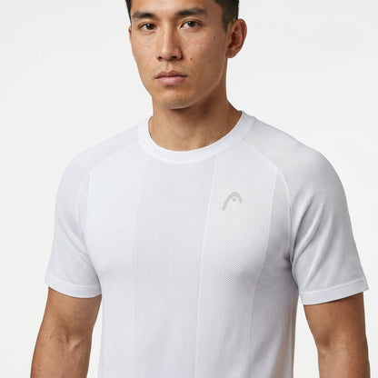 A man wearing a HEAD Performance Mens Tennis T-Shirt - White from HEAD, featuring short sleeves and a subtle chest logo, stands against a plain white background looking straight ahead with a neutral expression. This shirt is crafted with moisture-wicking fabric for comfort during intense tennis matches.