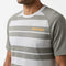 A person is wearing the HEAD Performance Mens Tennis T-Shirt - XPWG, a gray and white striped short sleeve athletic shirt from HEAD. Featuring bold orange “HEAD” lettering across the chest, this moisture-wicking tennis shirt is designed to deliver comfort and style for men both on and off the court. The individual’s face is not visible.