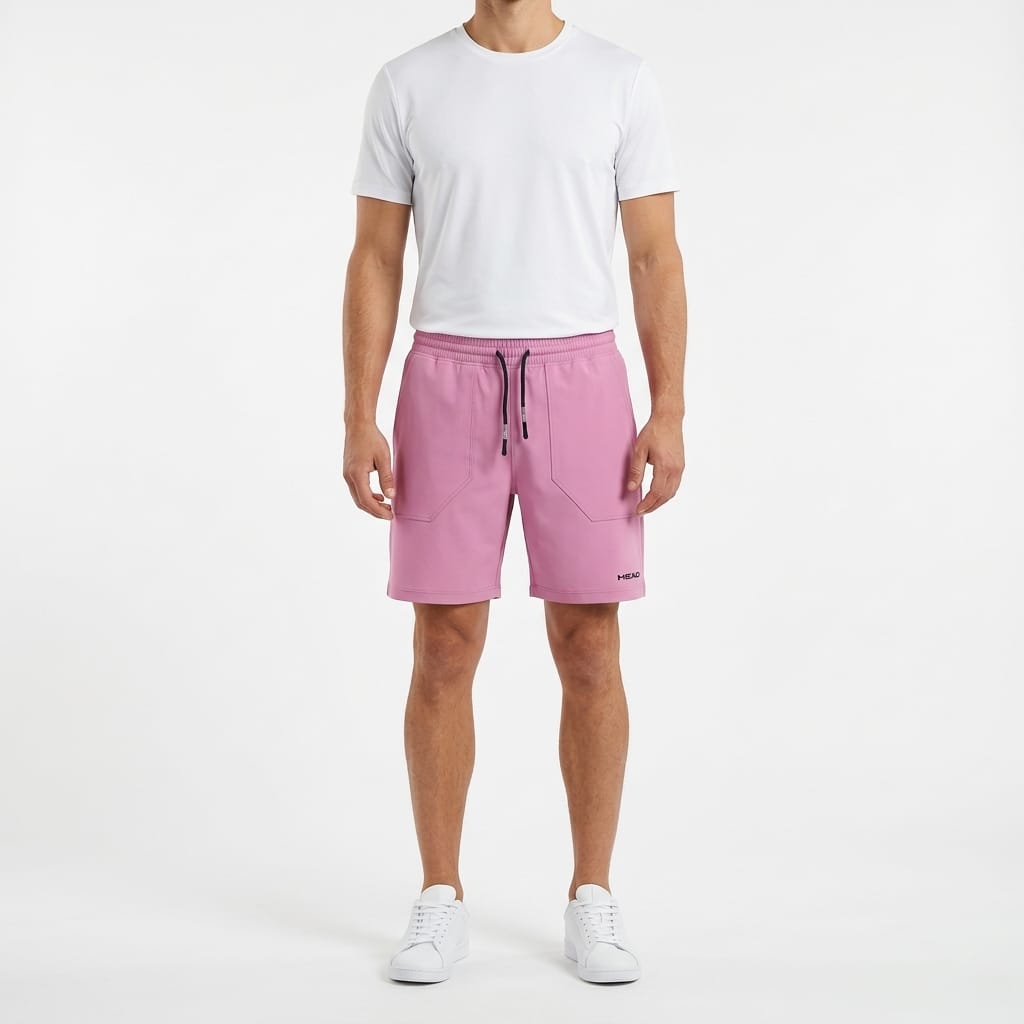 A person stands facing forward against a white background, wearing a plain white t-shirt, HEAD Performance Men’s Play Tennis Shorts in cyan pink by HEAD with a drawstring waist, and white sneakers.