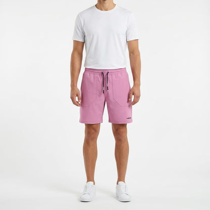 A person stands facing forward against a white background, wearing a plain white t-shirt, HEAD Performance Men’s Play Tennis Shorts in cyan pink by HEAD with a drawstring waist, and white sneakers.