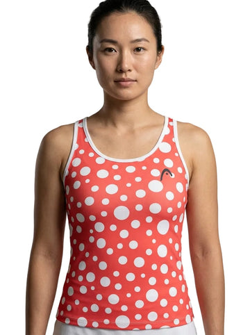 A person wearing the HEAD Spirit II Womens Tennis Tank Top - GIXR by HEAD, a sleeveless red top adorned with large white polka dots, stands against a plain white background, facing forward with a neutral expression. This stylish tank features advanced cooling technology and moisture transfer microfiber for ultimate comfort.