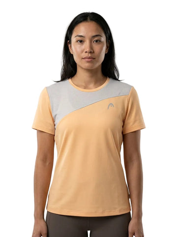 A woman with long dark hair is seen standing facing forward against a plain white background, wearing a HEAD Tie-Break Women’s Tennis T-Shirt (APLB) by HEAD in peach and gray.