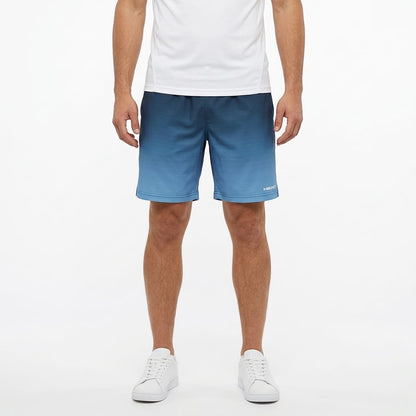 A man stands against a plain white background with his arms relaxed at his sides, wearing a white t-shirt, white sneakers, and HEAD Vision Power II Mens Tennis Shorts in Navy/Blue by HEAD, which feature 4-way stretch and moisture transfer microfiber.