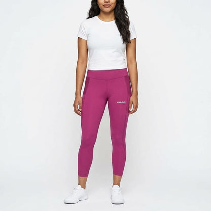 A woman stands against a white background wearing a white T-shirt, vivid pink HEAD Vision Women’s Tech Tennis Tights Leggings with the HEAD logo, and white sneakers. She has long dark hair and her arms rest by her sides.