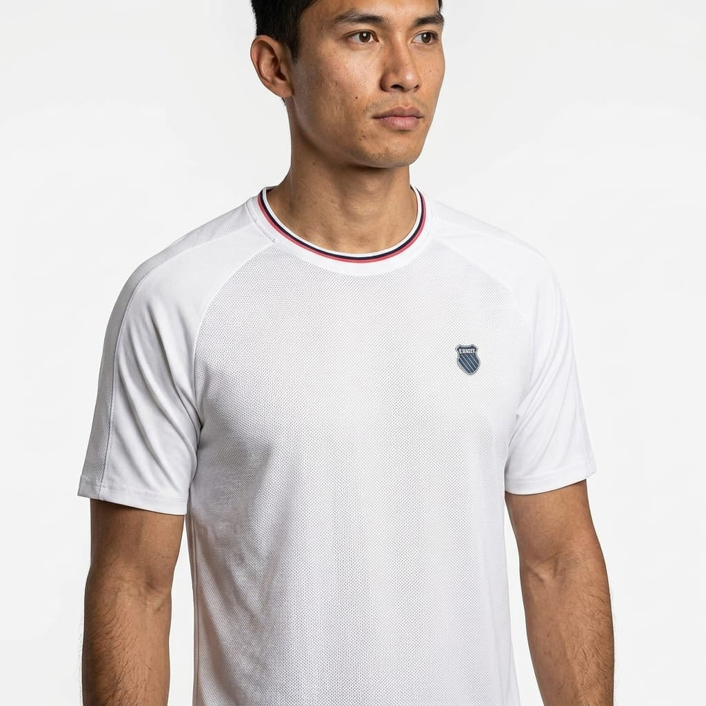 A man wearing the K-Swiss Hypercourt Mesh Crew 4 Mens Tennis T-Shirt in white—which features a small chest emblem and a red, white, and blue collar—stands against a plain white background. This classic K-Swiss tennis shirt embodies timeless style for men.