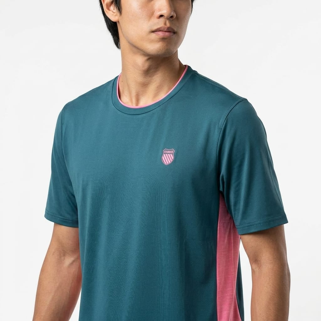A man wearing the K-Swiss Hypercourt Mix Melange Men’s Tennis T-Shirt in Stargazer/Pink, featuring a small pink emblem on the chest and pink side panels, stands against a white background.