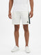 A man wearing a white t-shirt, Le Coq Sportif Pro Mens Tennis Shorts in Marshmallow—with a dark side stripe—and white sneakers stands against a plain white background. Designed by Le Coq Sportif for optimal comfort and movement, these breathable shorts are the ideal men’s tennis shorts for any active occasion.