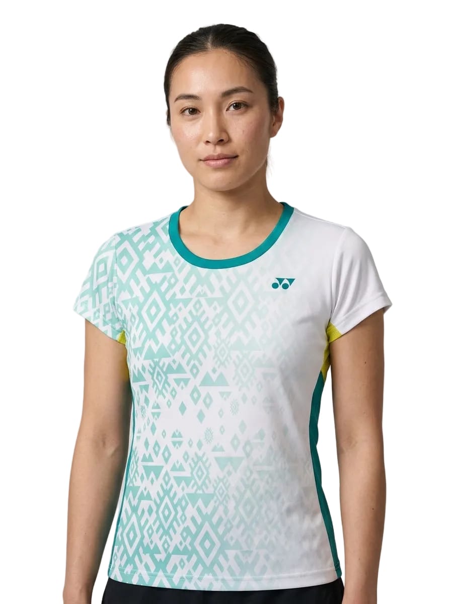 A person with long hair pulled back wears the Yonex YTL11 Women’s Tennis T-Shirt in white, a lightweight performance top by Yonex featuring short sleeves, teal geometric patterns, and yellow side accents, standing against a plain background.