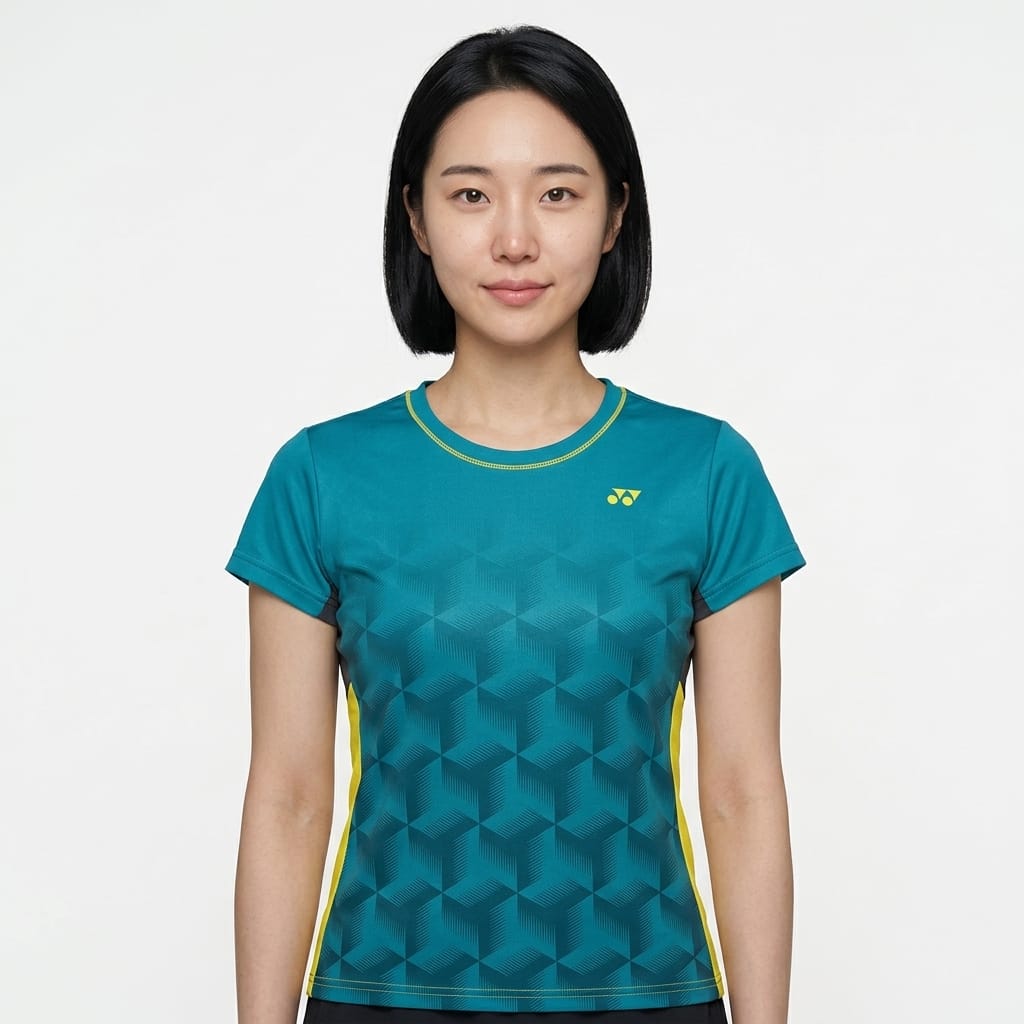 A woman with straight black hair wears the Yonex YTL12 Womens Tennis T-Shirt in teal—a stylish teal tennis shirt from Yonex featuring a geometric pattern and yellow accents—as she stands against a plain white background. Crafted from lightweight polyester, this top delivers comfort and style both on and off the court.