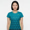 A woman with straight black hair wears the Yonex YTL12 Womens Tennis T-Shirt in teal—a stylish teal tennis shirt from Yonex featuring a geometric pattern and yellow accents—as she stands against a plain white background. Crafted from lightweight polyester, this top delivers comfort and style both on and off the court.