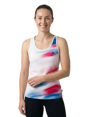 A woman with light skin and brown hair tied back stands smiling at the camera, wearing the HEAD Blur Women’s Tennis Tank Top - ROXU. The white tank top by HEAD features blue and red tie-dye patterns and is made from moisture-wicking fabric to keep her comfortable as she poses against a plain white background.