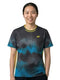 A person with long dark hair tied in a ponytail is wearing the Yonex YTL2025B Womens Tennis T-Shirt in black, featuring blue patterns and yellow accents on breathable sports fabric. She stands facing the camera and smiles against a plain white background.