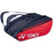 The Yonex 423212EX 12 Piece Racket Bag in Scarlet, featuring a red and black design with shoulder straps and branded logo, offers large zippered compartments that can accommodate up to 12 rackets along with additional sports equipment.