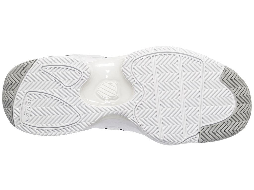 The image showcases the sole of a K-Swiss Defier RS men's tennis shoe in white and black, featuring a detailed tread pattern. The design seamlessly combines curved and straight lines to enhance stability and grip. The center displays the K-Swiss logo, while the heel section is designed with a durable herringbone pattern to ensure lasting performance.