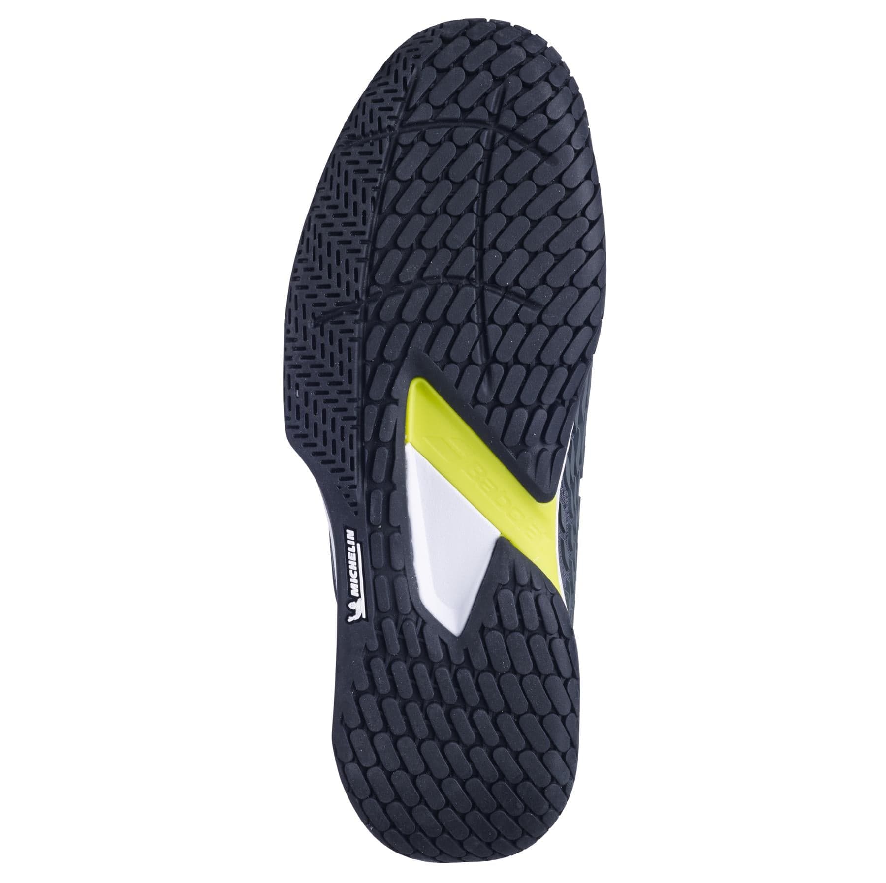 The image highlights the sole of a tennis shoe featuring a textured black tread pattern, with a striking yellow and white detail at its core, similar to the Babolat Propulse Fury 3 All Court Men's Tennis Shoes in Grey/Aero. These shoes ensure durability and traction thanks to their Power Belt feature.