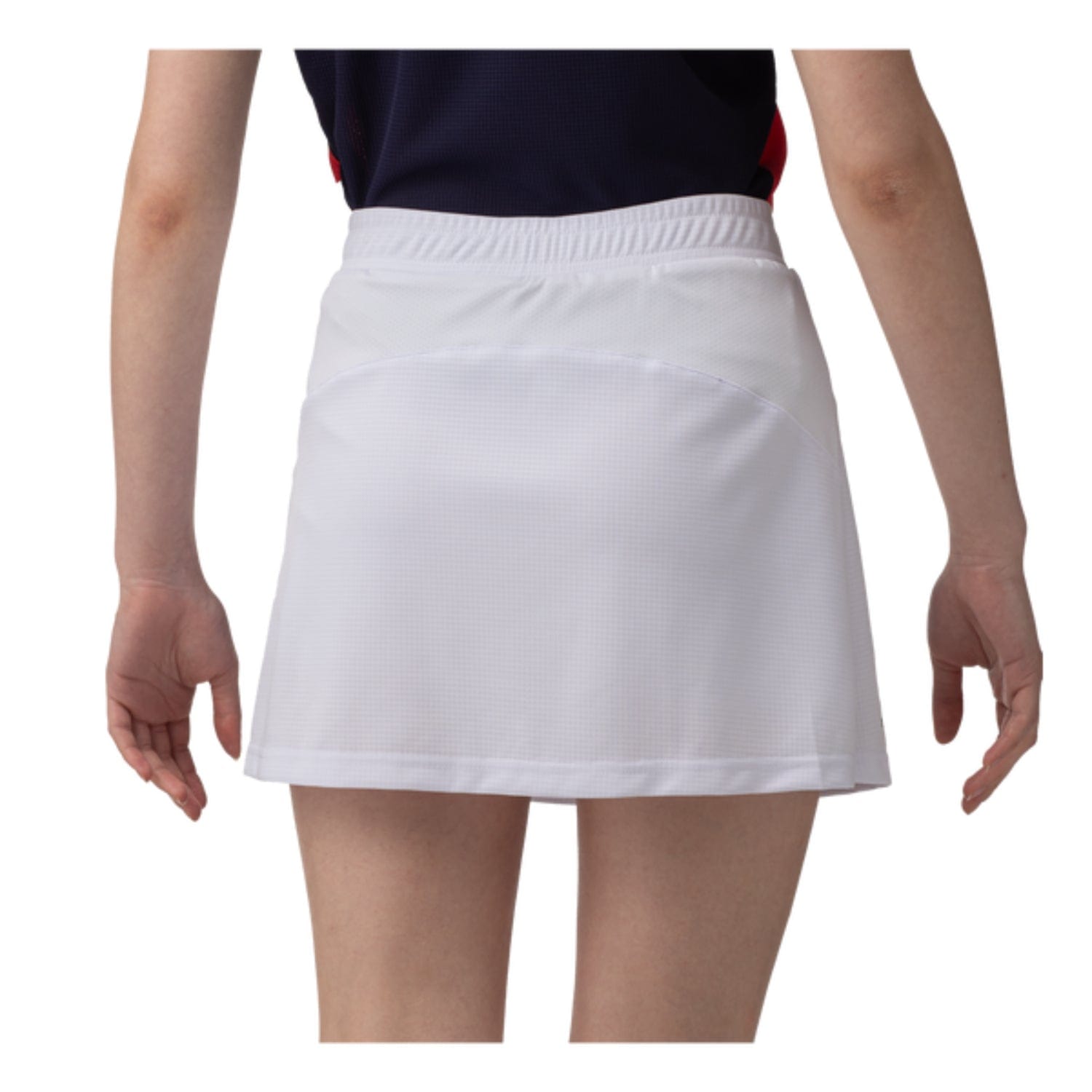 Rear view of a person wearing a navy top and the Yonex 26094 Women's Skort - White, standing against a plain background. This skort by Yonex showcases subtle texture with an elastic waistband and is designed with VERY COOL technology that offers UV reduction. The person's arms rest naturally at their sides.