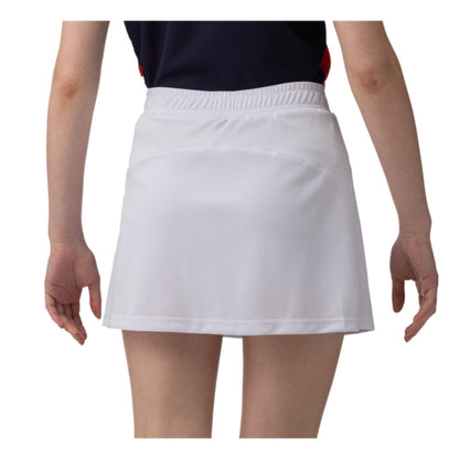Rear view of a person wearing a navy top and the Yonex 26094 Women's Skort - White, standing against a plain background. This skort by Yonex showcases subtle texture with an elastic waistband and is designed with VERY COOL technology that offers UV reduction. The person's arms rest naturally at their sides.