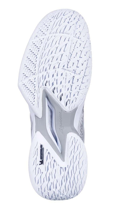 The image features the sole of a Babolat Jet Mach 3 All Court Men's Tennis Shoe in white and silver, showcasing a textured pattern for superior grip. Enhanced with Matryx Technology and multiple grooves, it includes gray accents in the middle area for extra support and shock absorption, optimizing performance.