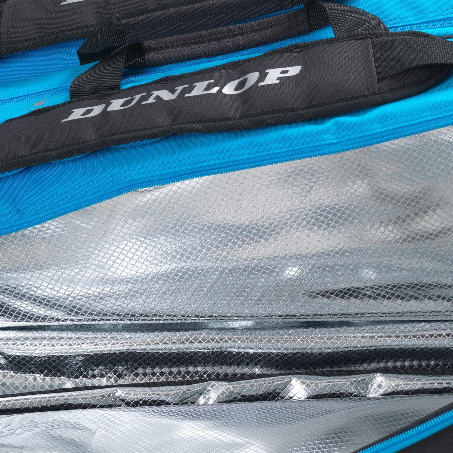 Close-up image of an open Dunlop FX Performance 12 Racket Thermo Tennis Bag - Black / Blue, showcasing its blue exterior and silver, reflective, insulated interior. The bag is partially unzipped to reveal the textured lining and specialized racket compartments that maintain a stable temperature for its contents.
