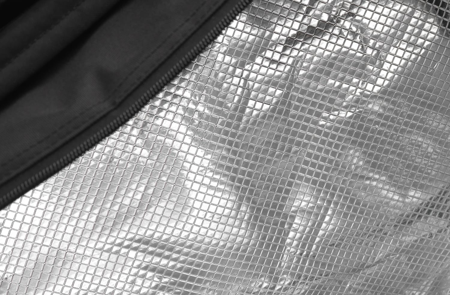 Close-up of a silver, reflective, metallic fabric featuring a grid-like pattern. A black zipper runs along the edge, contrasting with the textured surface. The material appears to be part of an insulated Dunlop CX Performance 12 Racket Thermo Tennis Bag in Black and Red.