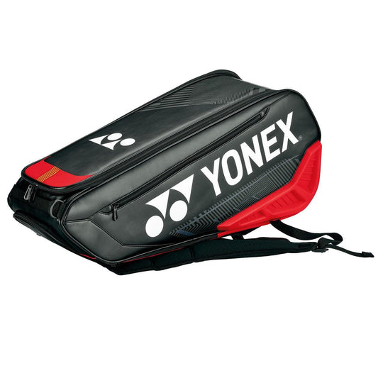 The Yonex 02326EX Expert 6 Piece Racket Bag - Black / Red boasts a sleek black design enhanced by red accents and a prominent white logo. It includes multiple zippered compartments and padded shoulder straps for comfortable carrying, along with a detachable laundry pouch for added convenience on the go.