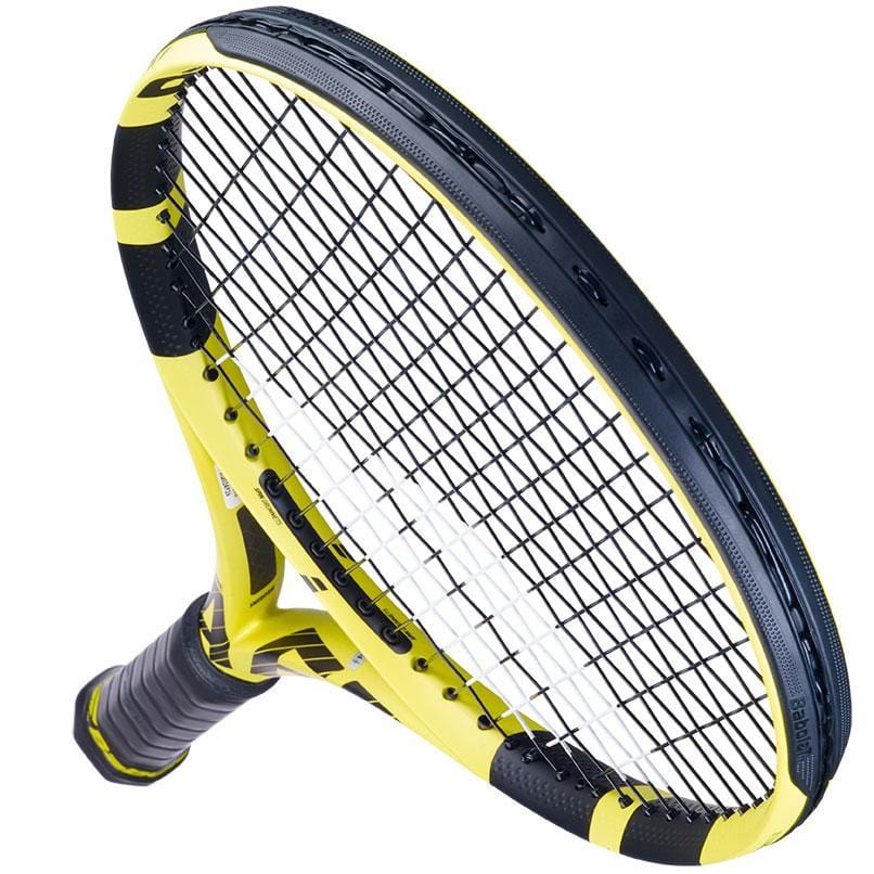 A Babolat Pure Aero + Tennis Racket in yellow and black, with a grid of closely strung strings and a textured grip, is featured diagonally against a white background. It showcases its aerodynamic frame designed to enhance spin and control through its modern aesthetics.
