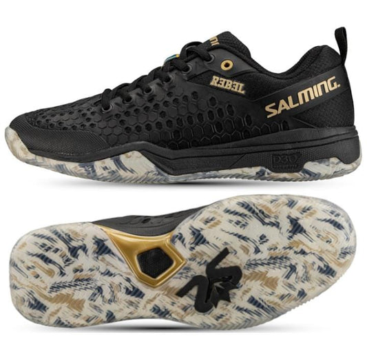 A pair of Salming Rebel Men's Indoor Court Shoes in black and gold, featuring a honeycomb texture. The shoes are designed for stability and grip, with soles accented in white, gray, and gold. The brand "Salming" is displayed in gold, while the model name is imprinted on the side in yellow.