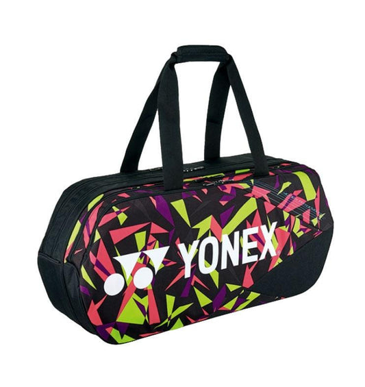 The Yonex 92231WEX Pro Tournament Bag - Smash Pink features a vibrant geometric pattern with green, pink, and yellow shapes set against a black background. This professional-quality sports bag is equipped with dual black handles and prominently displays a white Yonex logo.