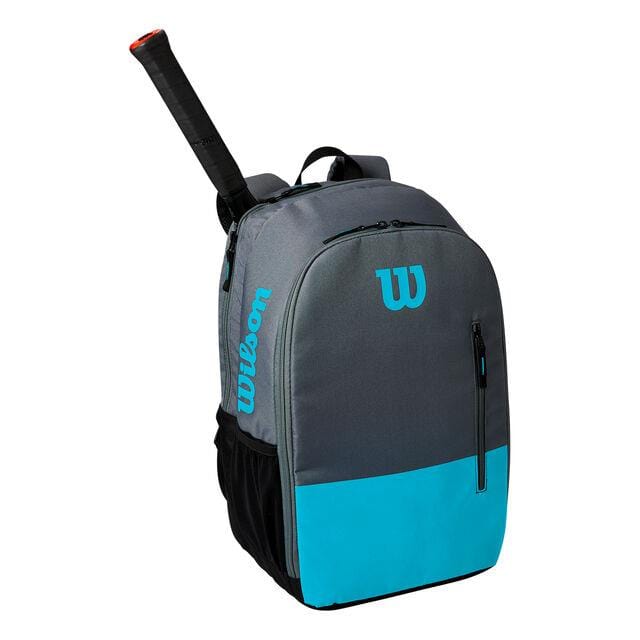 The Wilson Team Collection Tennis Backpack in Blue and Grey showcases a unique racket pocket with the handle visible from the top compartment. It features a side pocket and prominently displays the iconic Wilson logo in blue.
