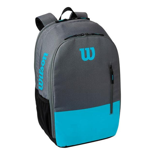 The Wilson Team Collection Tennis Backpack in Blue and Grey prominently displays the brand's iconic "W" logo and name on the front. It includes a racket pocket, a front zipper pocket, a side mesh pocket, and two shoulder straps for added convenience.