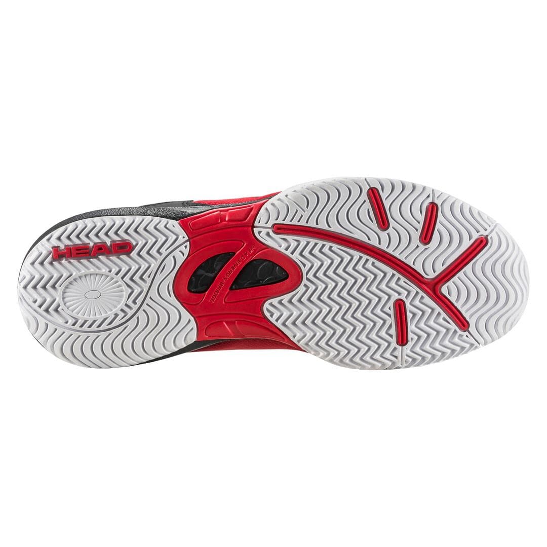 The image displays the sole of a HEAD Sprint 3.5 Junior Tennis Shoe in red and black, highlighting a wavy tread pattern designed for superior grip. Constructed with non-marking rubber and breathable mesh, this shoe offers exceptional traction on the court. The brand name "HEAD" is prominently featured on the heel area.